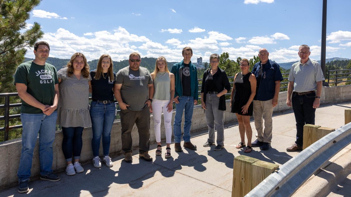 After giving final presentations, SURF's 2022 interns stand with SURF staff and the Bauer family, with the Ross Headframe in the background. From left to right, Curtis Petersen, Jacquelynn McKnight, Reghan DeBoer, Chad Ronish, Lindsey Weeldreyer, Joseph Egan, Julie Bauer, Julie Bauer, Steve Bauer, Mike Headley. Photo by Matthew Kapust.